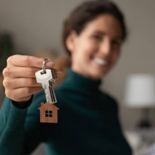 Close up focus on keys, smiling woman Real Estate Agent selling apartment, offering to client, showing at camera, holding documents, contract, making purchasing deal, real estate agent, mortgage or rent