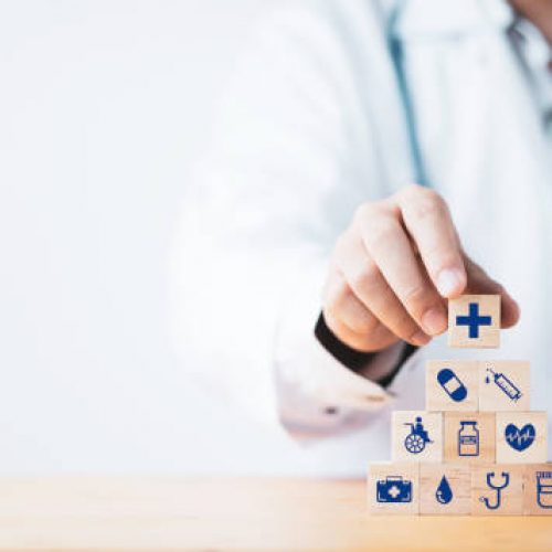Doctor putting and stacking wooden block cube which print screen health care and medical icons for healthy and wellness concept.